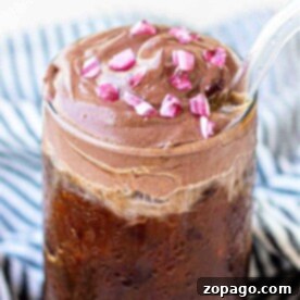 Iced coffee topped with a layer of thick, peppermint chocolate cream cold foam and pink sprinkles, served with a clear straw.