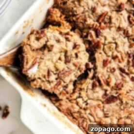 A close-up of a sweet potato dump cake-inspired pecan cobbler in a white baking dish, complete with a rustic wooden spoon.
