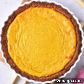 Pumpkin Custard Pie in a white dish with a brown crust, next to a pink cloth and utensils.
