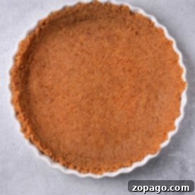 Graham cracker crust for cheesecake elegantly nestled in a fluted tart pan rests on a gray surface, ready to charm with its simplicity and flavor.