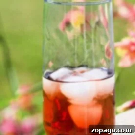 A tall glass of sun tea, made from a cherished recipe, with ice cubes clinking, sits on a wooden surface outdoors as vibrant flowers softly blur in the background.