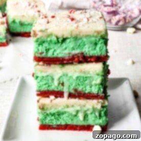 A delightful dessert lasagna of green and red layered cheesecake bars sits atop a sugar cookie crust, crowned with white frosting and sprinkled with crushed peppermint.