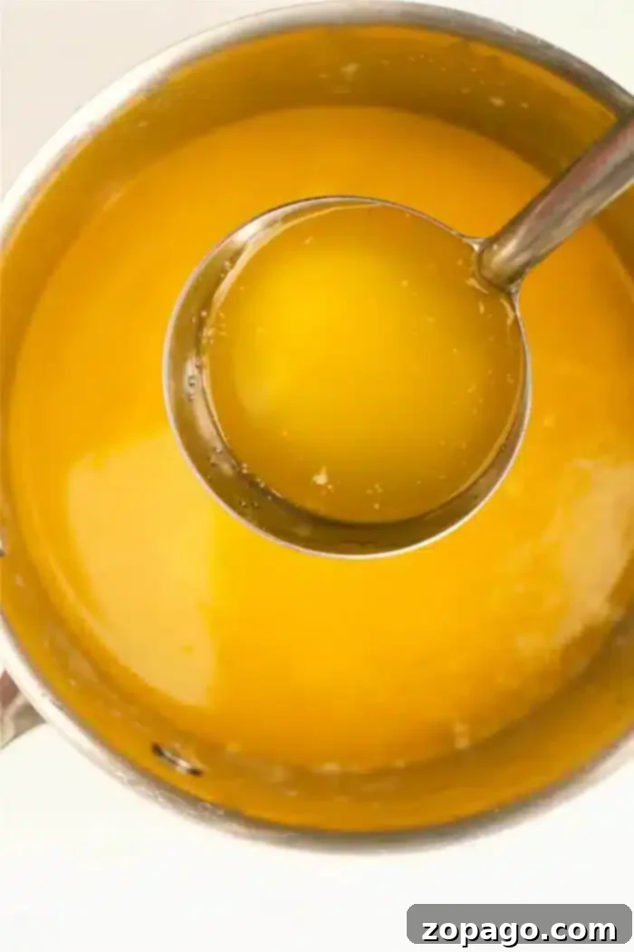 Mastering Clarified Butter 2 A metal pot brimming with golden liquid butter, with a silver ladle partially lifted out, showcasing its rich, pure essence.