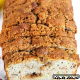A loaf of banana bread with a crumbly topping, partially sliced, showcases a delightful twist on the classic banana bread recipe using no butter.