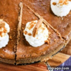 Gingerbread cheesecake with a gingersnap crust, topped with whipped cream and cookie crumbles, elegantly presented on a wooden board alongside neatly arranged slices.