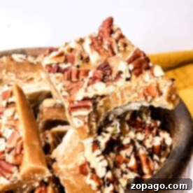 Close-up of a wooden bowl filled with pieces of pecan praline fudge. The pralines, topped with chopped pecans, showcase their rich, caramelized texture. The bowl rests on a white surface with a hint of a yellow cloth in the background.