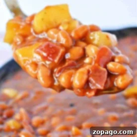Close-up of a spoonful of apple pie baked beans with diced yellow peppers and tomatoes in a thick sauce.