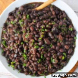 A bowl of black turtle beans cooked to perfection, garnished with chopped herbs, and elegantly served with a wooden spoon. Discover how to cook these delightful beans and elevate your culinary experience.