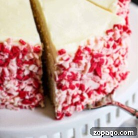Peppermint Cake with white frosting and red and white peppermint chunks on the sides, elegantly presented on a white cake stand.