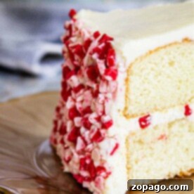 A slice of white cake with peppermint frosting and red and white sprinkles sits elegantly on a plate.