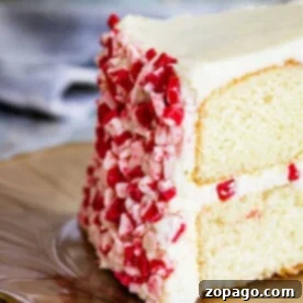 A slice of white cake with peppermint frosting and red and white sprinkles sits elegantly on a plate.