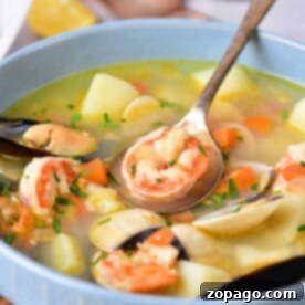 A bowl of shrimp and corn soup brimming with mussels, potatoes, and carrots, garnished with fresh herbs, and accompanied by a spoon.