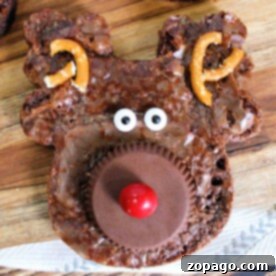 Santa's Favorite Brownies 7 Reindeer-shaped Christmas brownies adorned with pretzel antlers, candy eyes, and a red nose rest on a wooden surface.