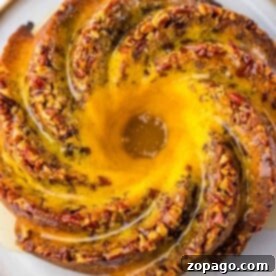 Pecan Bundt cake swirled to perfection, topped with chopped nuts, drizzled with glaze, elegantly presented on a round plate.