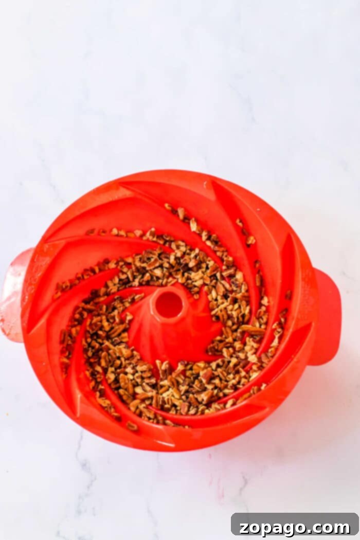 Decadent Pecan Bundt 8 The fully assembled and beautifully glazed Pecan Bundt Cake, generously garnished with extra pecans, presented on a rustic wooden cake stand, making it a perfect centerpiece dessert for any festive occasion or family gathering.