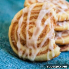 A tempting stack of cinnamon roll cookies with icing sits invitingly on a blue cloth background, one partially eaten.