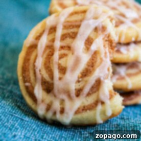 A tempting stack of cinnamon roll cookies with icing sits invitingly on a blue cloth background, one partially eaten.