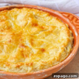 Golden-brown pie with a delectable sourdough pie crust in a round, orange baking dish on a light surface, accented by a checkered cloth in the background.