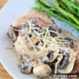 Creamy mushroom chicken, infused with Chicken and Cream of Mushroom Soup, topped with cheese, served alongside asparagus on a white plate.