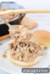 A spoon serving creamy Big Mac Sloppy Joes, with a skillet and more buns in the background.