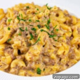 A plate of creamy hamburger mac and cheese with ground beef, garnished with chopped parsley.