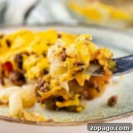 Fork with cheesy hamburger casserole, featuring ground beef, cheese, vegetables, and a hint of cabbage on a plate.