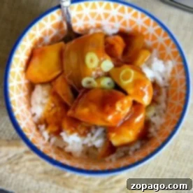 A colorful bowl of crockpot orange chicken topped with sliced green onions, with a fork inside.