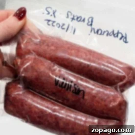 A hand holds a vacuum-sealed pack of three venison sausages labeled with a date and Venison Sausage Recipe notes in blue marker.
