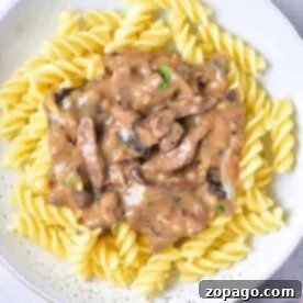 A plate of spiral pasta topped with creamy venison stroganoff, garnished with a sprig of parsley.
