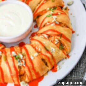 Buffalo chicken crescent roll taco ring drizzled with hot sauce, garnished with blue cheese and chives, with dipping sauce in the center.