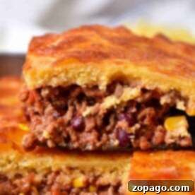 A close-up of a layered jiffy chili cornbread casserole, featuring ground meat filling and visible corn and beans.