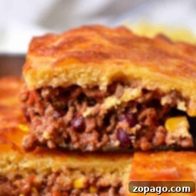 A close-up of a layered jiffy chili cornbread casserole, featuring ground meat filling and visible corn and beans.