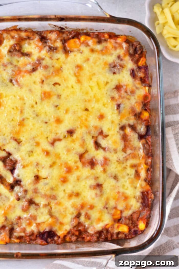 Hearty Taco Cornbread Bake 6 A Jiffy taco cornbread casserole topped with melted cheese in a glass dish, accompanied by sliced cheese on the side.