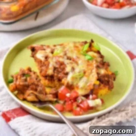 Taco cornbread casserole on a plate with a side of diced tomato salad, resting on a cloth napkin.
