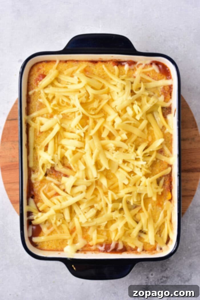 A wooden board cradles a casserole dish brimming with cornbread casserole, topped with golden melted cheese, reminiscent of a comforting Mexican cornbread casserole.