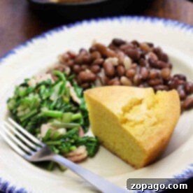 A plate featuring savory beans and cornbread alongside fresh greens, with a fork set neatly on the side.