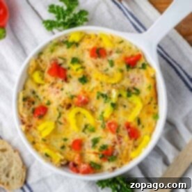 A delicious baked dish of Rotel Sausage Dip with melted cheese, peppers, and herbs in a white pan on a cloth, perfectly paired with a fresh baguette nearby.
