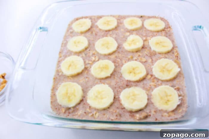 Golden Banana Bread Baked Oats 4 A glass baking dish with Banana Oatmeal batter, topped with banana slices, ready to be baked.