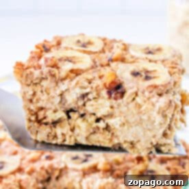 A spatula lifts a square of Banana baked Oatmeal, topped with fresh banana slices and crunchy nuts.