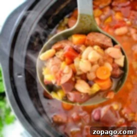 A ladle scoops hearty 15 Bean Soup with sausage from a crock pot.
