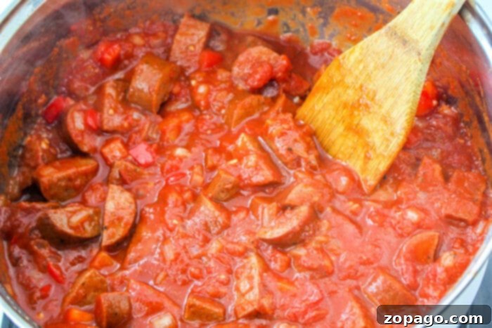 Hearty Sausage Spaghetti 7 A pot of chunky tomato sauce with sausages sits invitingly, its rich aroma filling the air. Next to it, a wooden spoon rests, ready to twirl into a perfect blend reminiscent of sausage spaghetti.