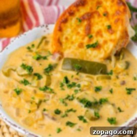A bowl of hearty steak and potato soup, infused with creamy goodness and vegetables, topped with cheesy bread and garnished with herbs.