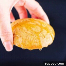 Golden Cornbread Cookies 7 A hand holds a cornbread cookie drizzled with honey, set against a dark background.