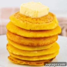 A stack of golden fried cornbread, topped with butter on a pristine white plate.