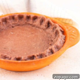 A rich chocolate pie crust sits elegantly in a ceramic dish on a beige surface, complemented by a soft cloth in the background.