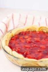 Cherry pie with a cinnamon roll pie crust spiraled uniquely in a glass dish, set on a light surface with a striped towel in the background.