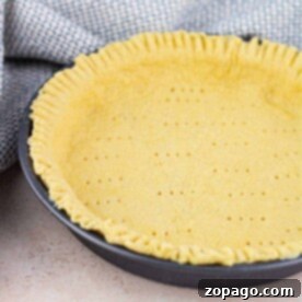 A Bisquick pie crust sits in a round black pan with crimped edges, perfectly complementing the nearby textured cloth.