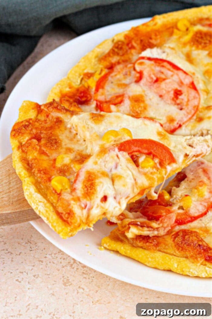 Crispy Cornmeal Pizza Crust 2 Close-up of a cheesy pizza slice with tomatoes on a cornmeal pizza crust being lifted from the whole pie on a white plate, highlighting the crispy texture.