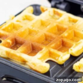 Close-up of a golden cornmeal waffle cooking in a waffle maker, with crisp edges and the classic square pattern clearly visible.