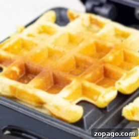 Crispy Cornmeal Waffles 9 Close-up of a golden cornmeal waffle cooking in a waffle maker, with crisp edges and the classic square pattern clearly visible.